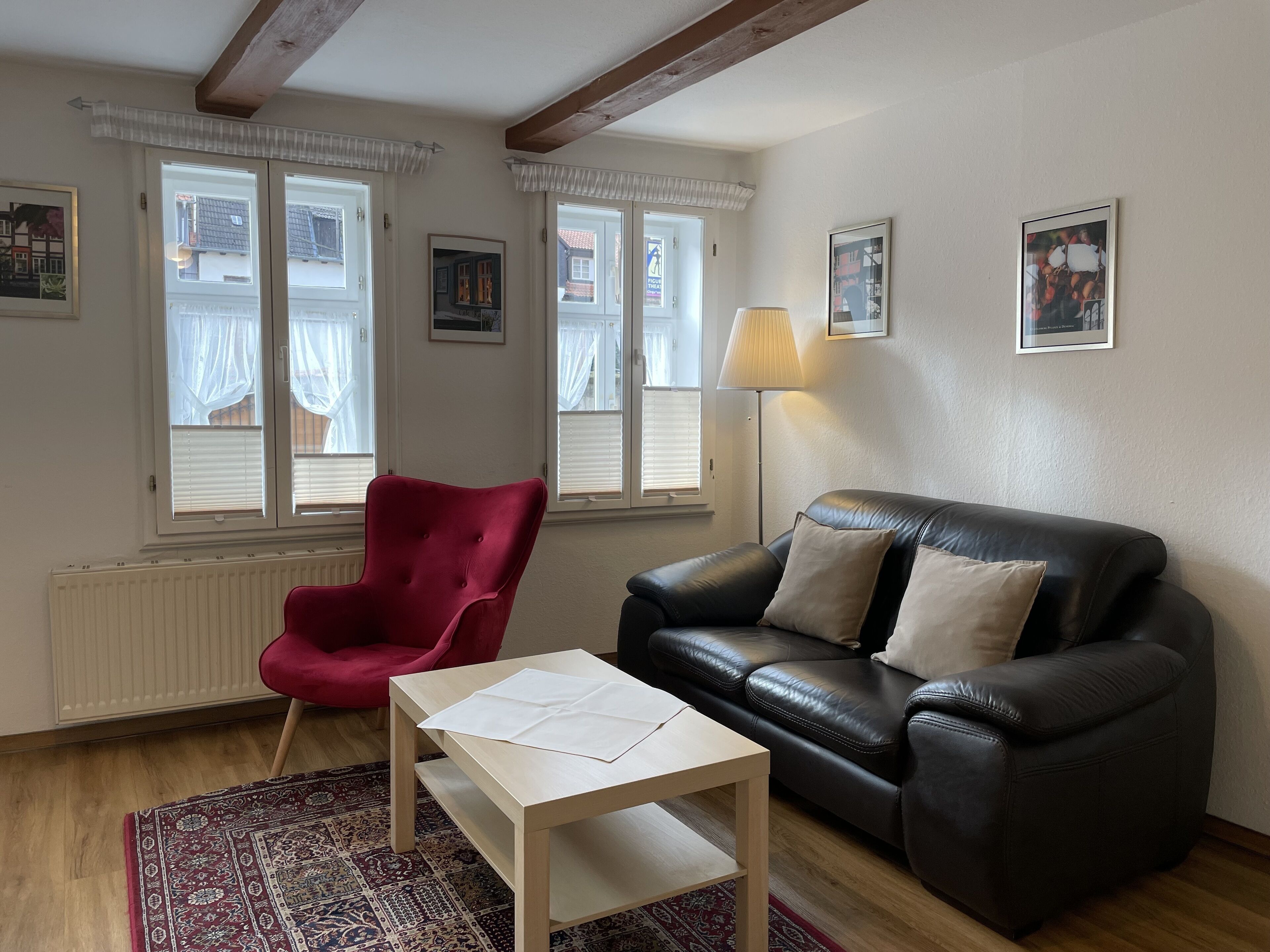 A living room with a red armchair, a black leather sofa, a wooden coffee table, and a patterned rug.