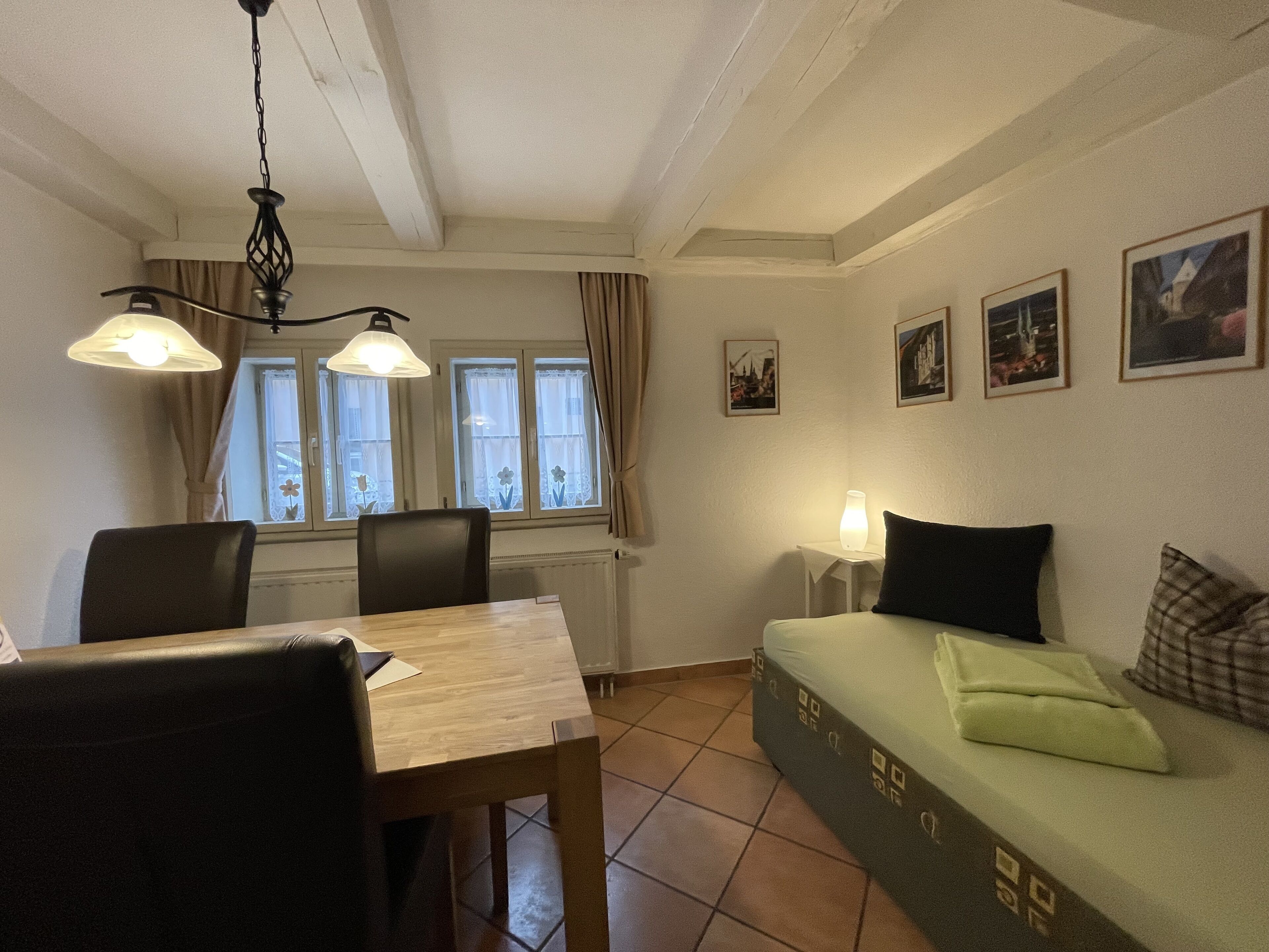Um quarto aconchegante com uma mesa de jantar, cadeiras, um sofá com almofadas, uma mesinha de cabeceira com abajur e quadros nas paredes.