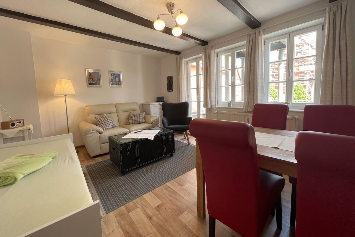 A living room with a sofa, a table, chairs, a lamp, and a suitcase.