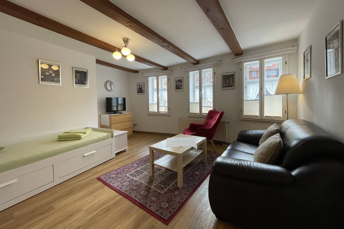 A living room with a sofa, a red chair, a TV on a dresser, and a ceiling fan.