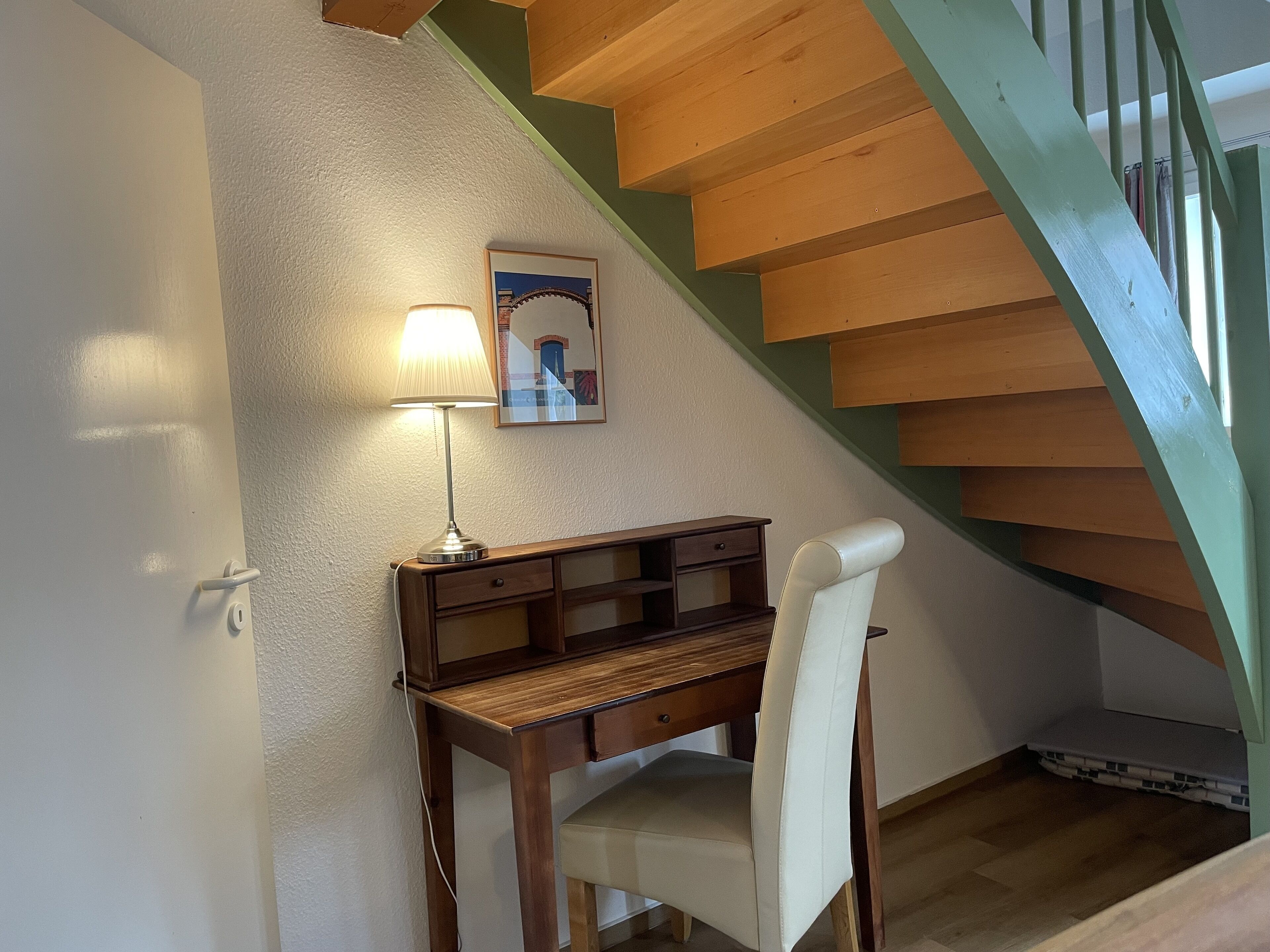 Quarto com escrivaninha, cadeira, abajur e um quadro na parede.