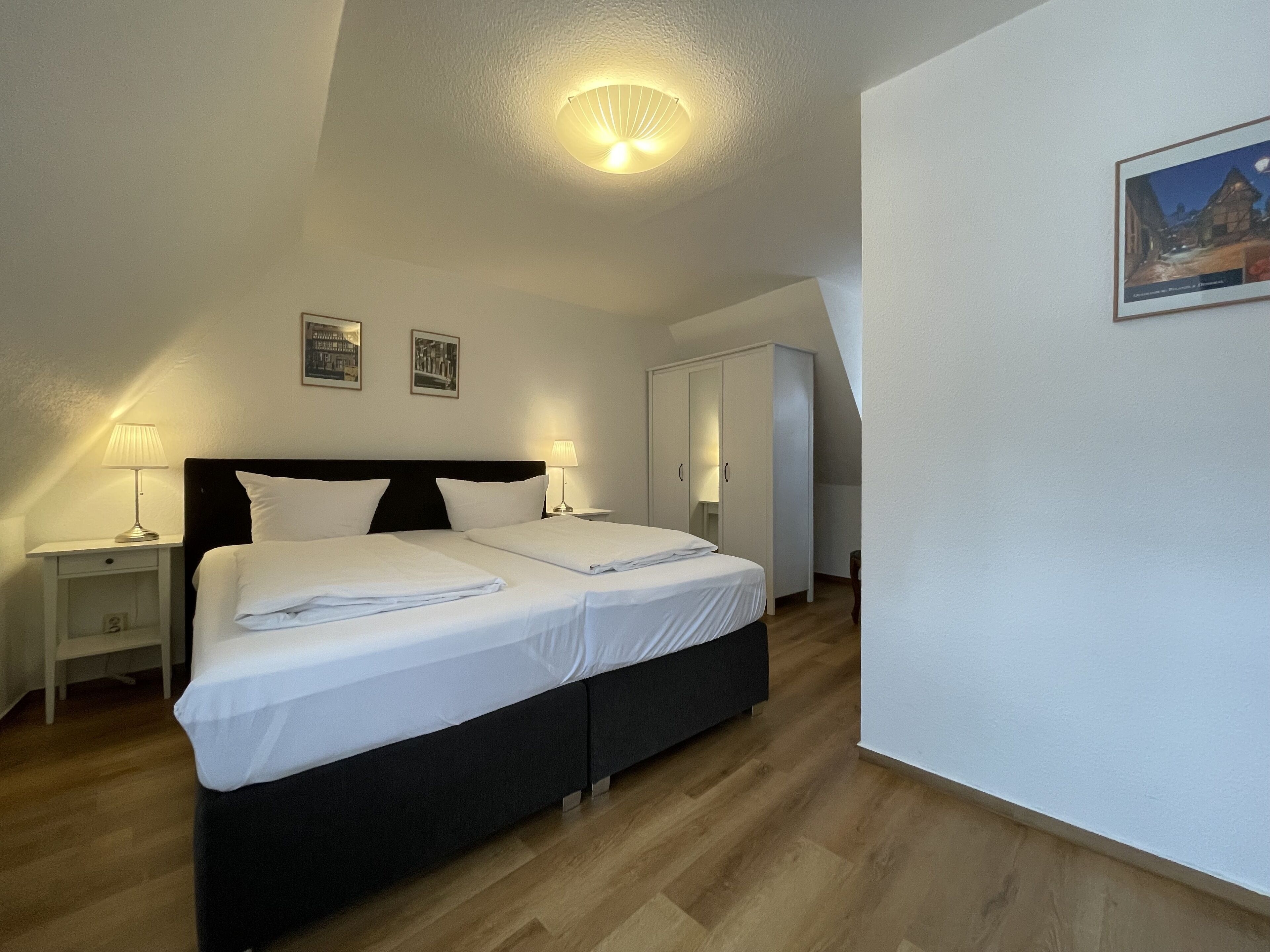 A bedroom with two beds, a nightstand, a lamp, and a framed picture on the wall.