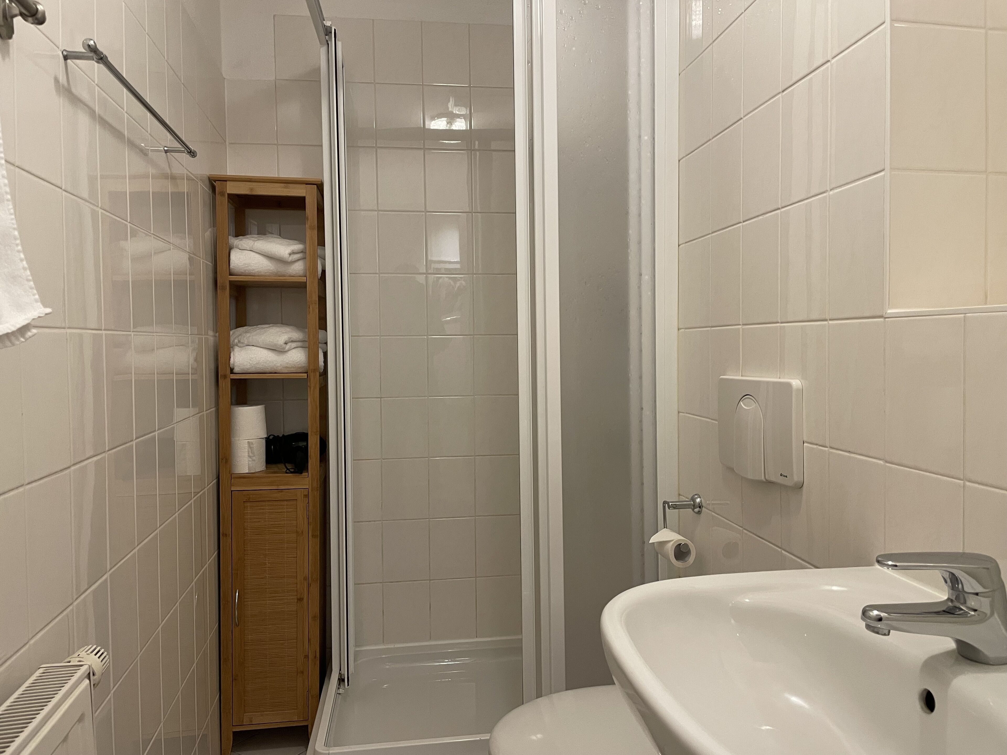 Ein Badezimmer mit Dusche, einem Holzboden mit Handtüchern, einem Toilettenpapierhalter und einem Waschbecken.