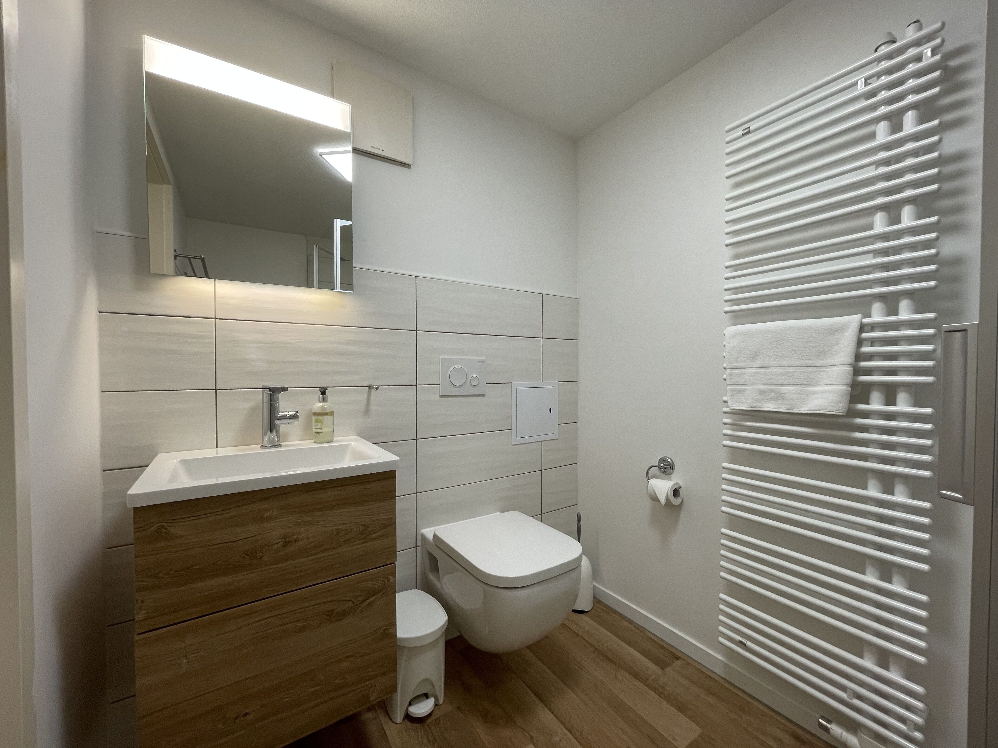 Ein modernes Badezimmer mit einem Holz-Waschtisch, einer Toilette und einem Handtuchhalter.