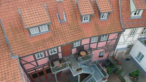 A multi-story building with a red-tiled roof, a central courtyard with a round table, and a staircase leading to an upper floor. - Urlaub im Fachwerk (Quedlinburg)