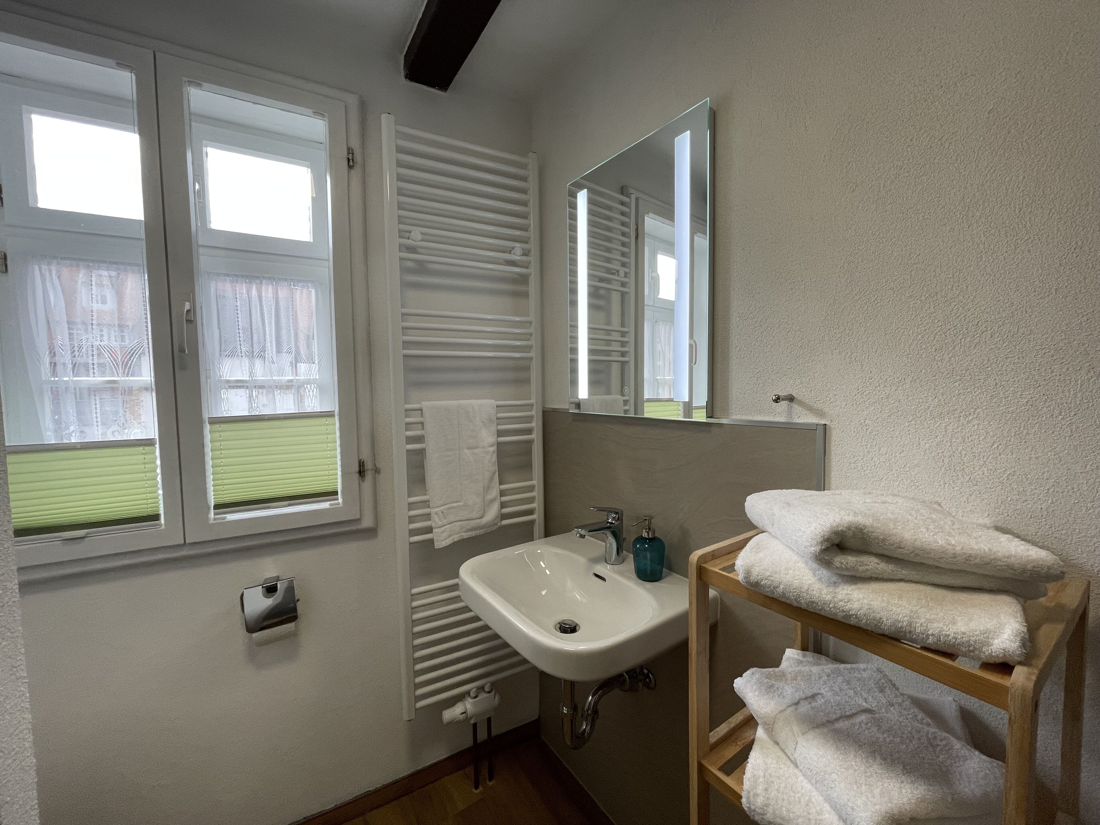 Un baño con ventana, lavamanos, espejo y toallero.