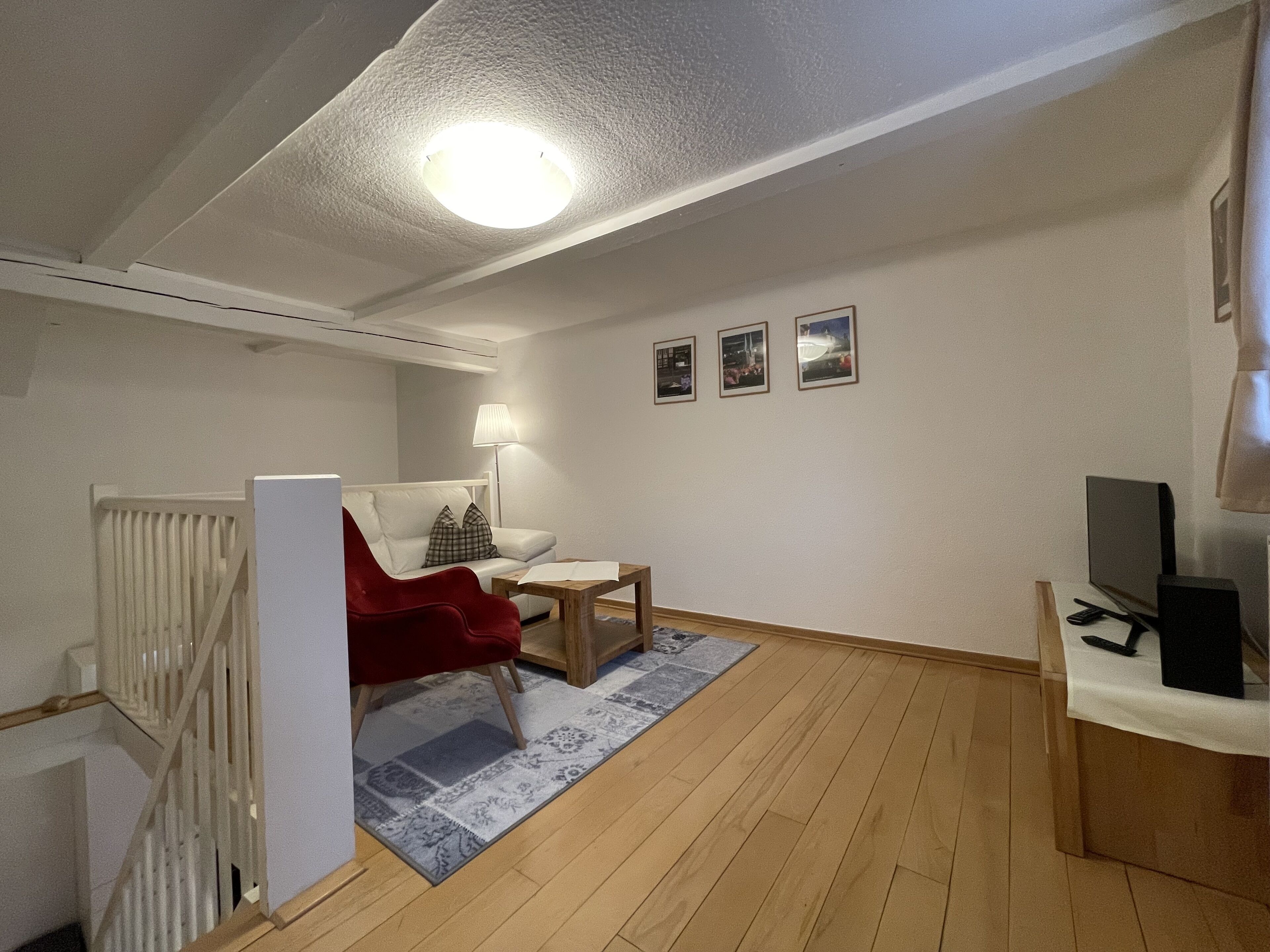 Un salon moderne avec un fauteuil rouge, une petite table, une lampe et un téléviseur.