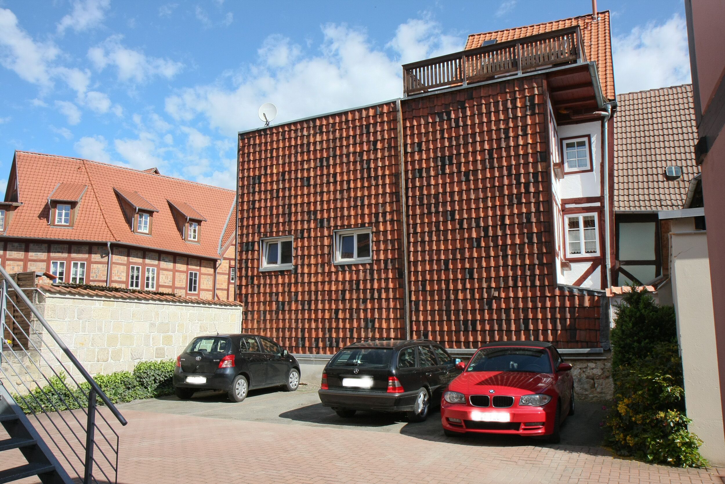 A building with a tiled facade, a staircase leading to an entrance, and three parked cars.