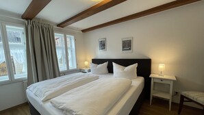 A neatly made bed with white linens, a wooden headboard, and a bedside table with a lamp. - Urlaub im Fachwerk (Quedlinburg)