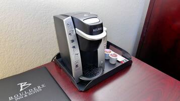 Una máquina de café Keurig sobre una mesa de madera con un folleto del Boulders Inn & Suites.
