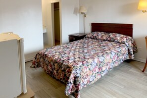 A bedroom with a floral bedspread, a wooden headboard, a bedside table with a lamp, and a wardrobe.