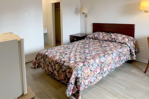 Un dormitorio con una colcha estampada con motivos florales, un cabecero de madera, una mesita de noche con una lámpara y un armario.