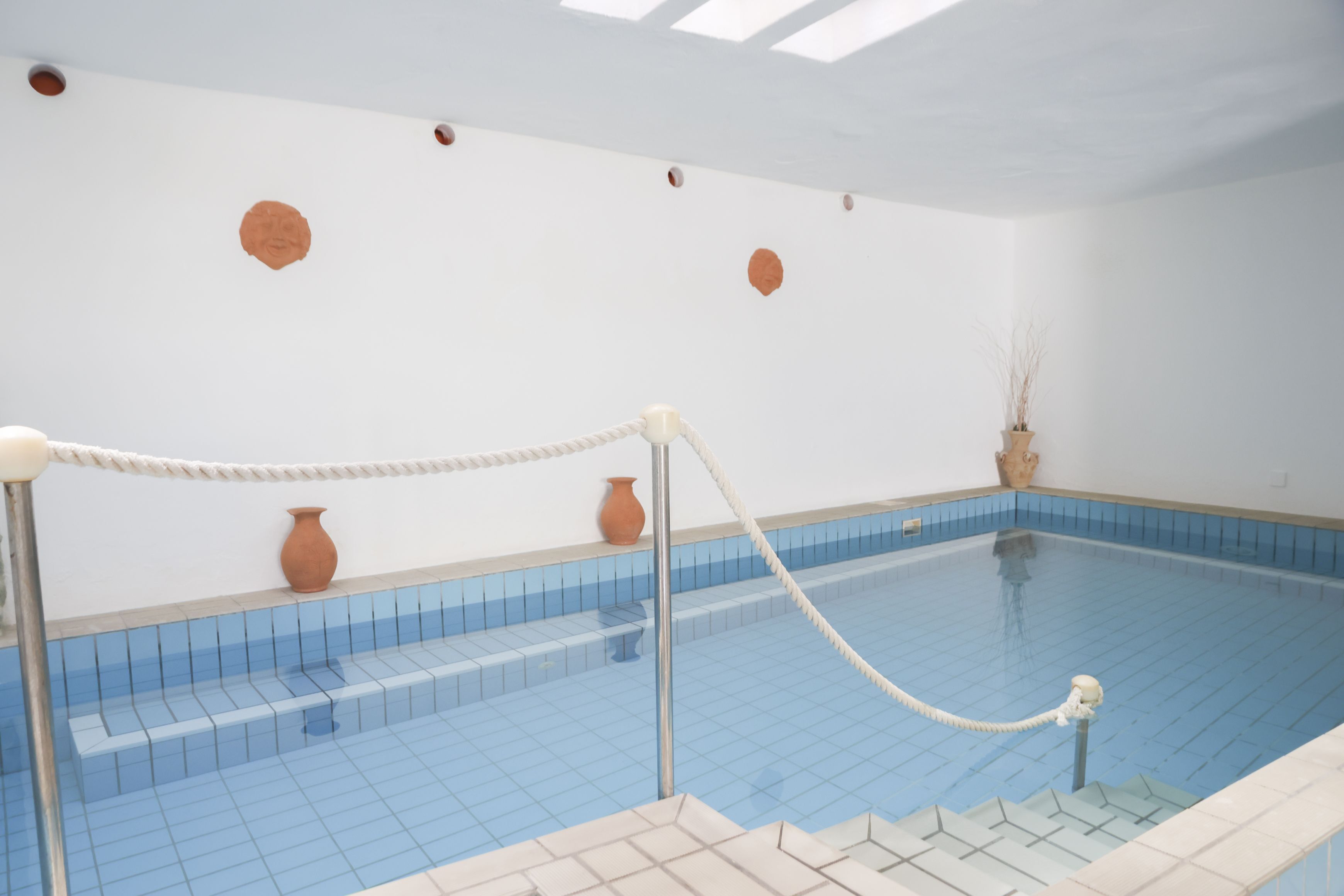 A swimming pool with a rope barrier, tiled walls, and a few decorative vases.