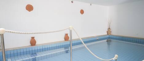 A swimming pool with a rope barrier, tiled walls, and a few decorative vases.