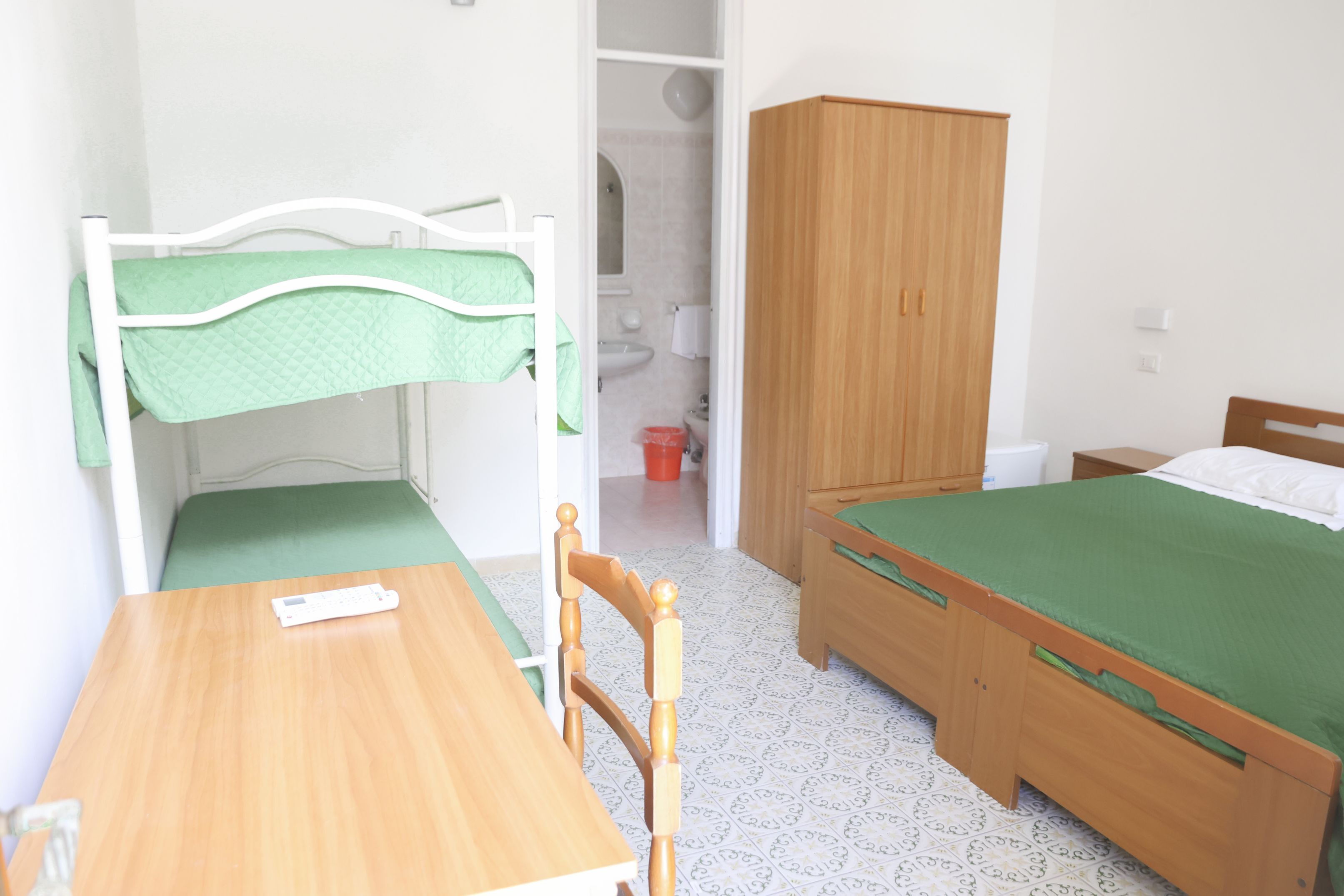A bedroom with a bunk bed, a single bed, a wooden wardrobe, a table, and a chair.