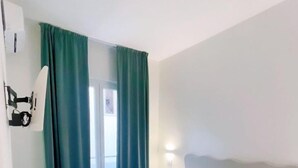 A hotel room with a bed, a nightstand, a wall-mounted lamp, and a sliding door with curtains. - Hotel Cesotta (Forio)