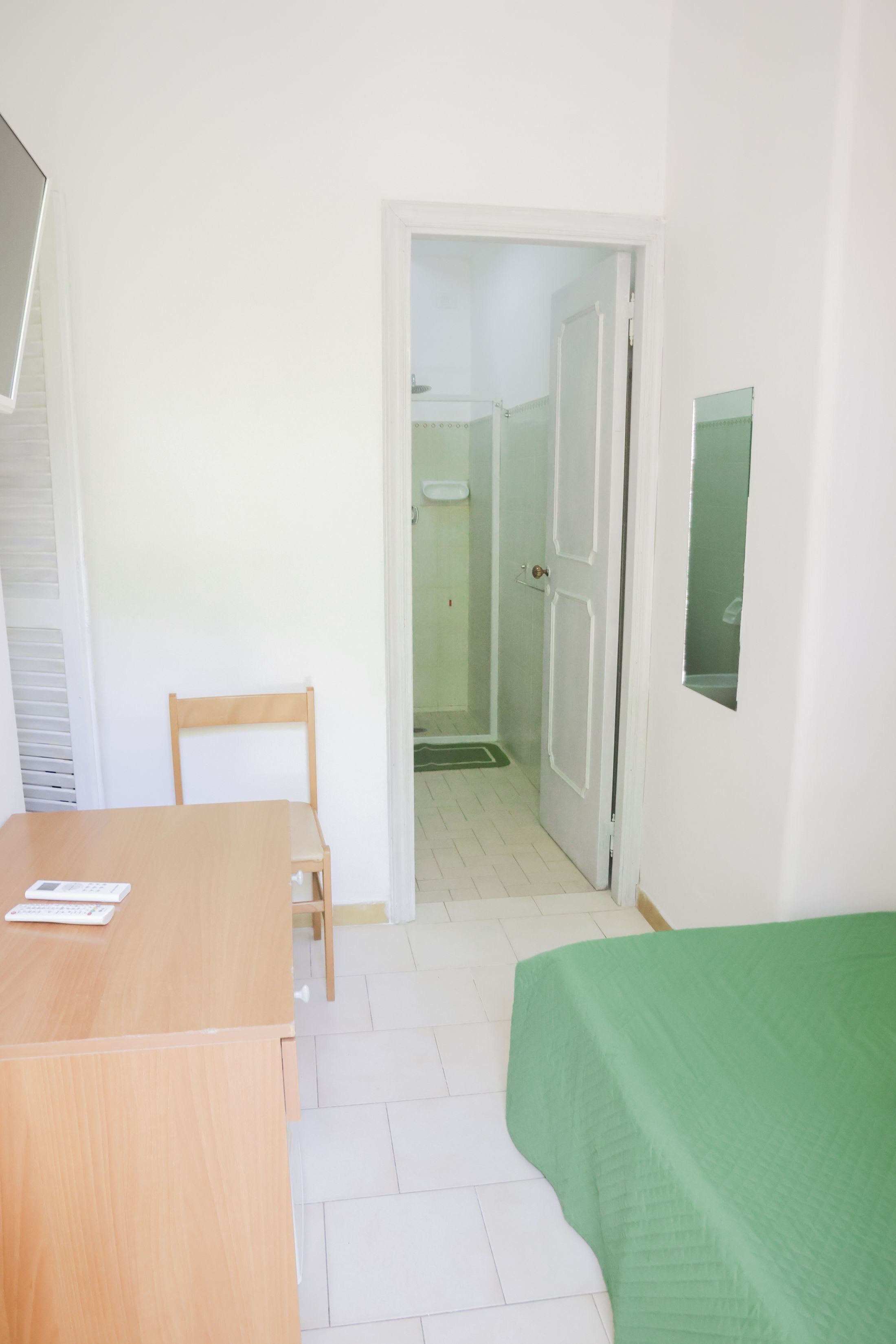 Una habitación con un escritorio de madera, una cama verde, una silla y una puerta que da a un baño.