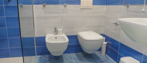 A bathroom with a bidet, toilet, sink, and a trash bin.