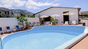 A swimming pool with lounge chairs and umbrellas, surrounded by a white building with a tiled pool edge. - Hotel Cesotta (Forio)