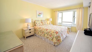 A bedroom with a bed, two bedside tables with lamps, a window with curtains, and a television on a dresser. - Ocean Hideaway 607 by RedAwning (Ocean City)