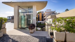 A modern building with a curved roof, glass entrance, and potted plants. - Zeus Residence Hotel (Aci Castello)