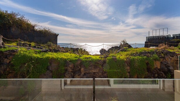 A modern building with a glass facade overlooking a rocky coastline and ocean. - Zeus Residence Hotel (Aci Castello)