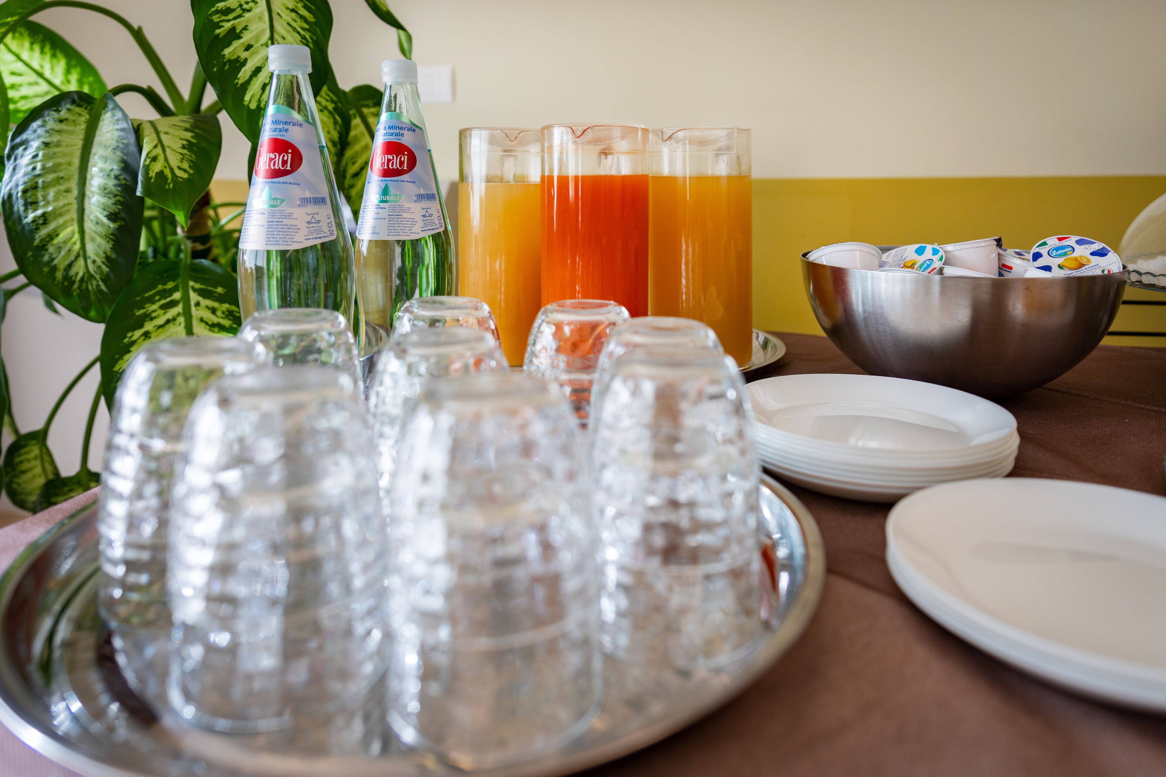 Una bandeja con varios vasos, un bol con platos y botellas de agua.