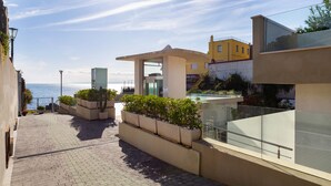 A rooftop terrace with a clear view of the sea, a glass balustrade, and a modern building with a yellow facade. - Zeus Residence Hotel (Aci Castello)