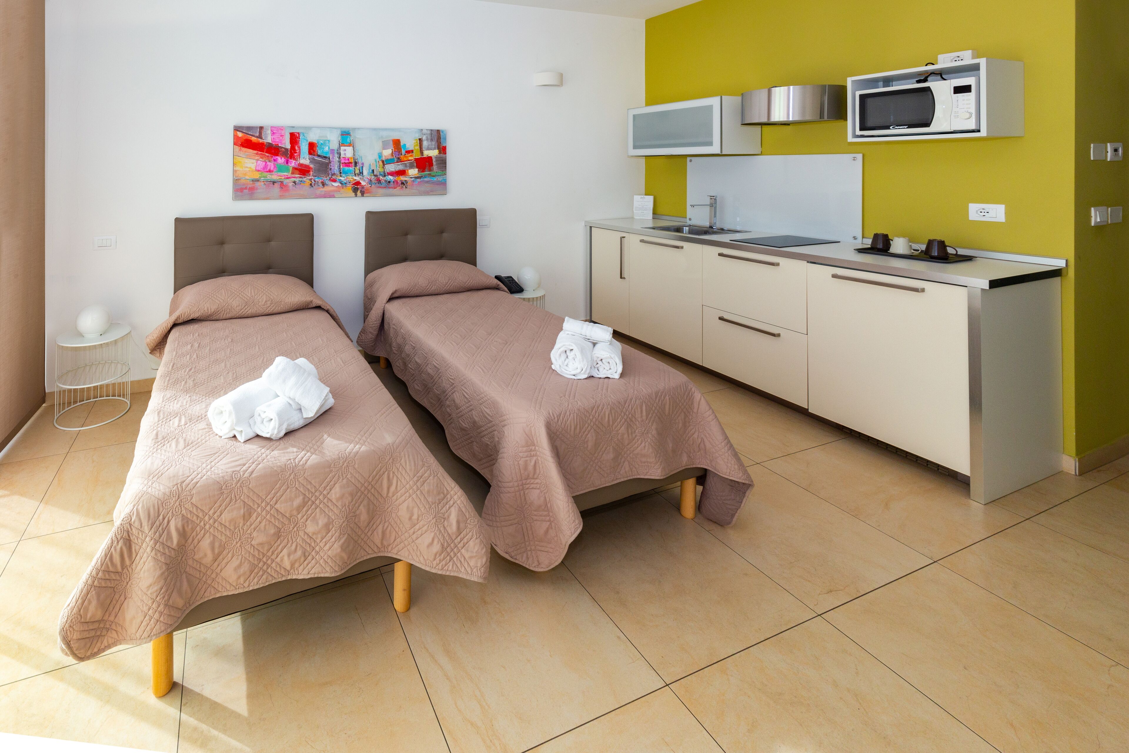 Habitación de hotel con dos camas, una kitchenette y un cuadro en la pared.