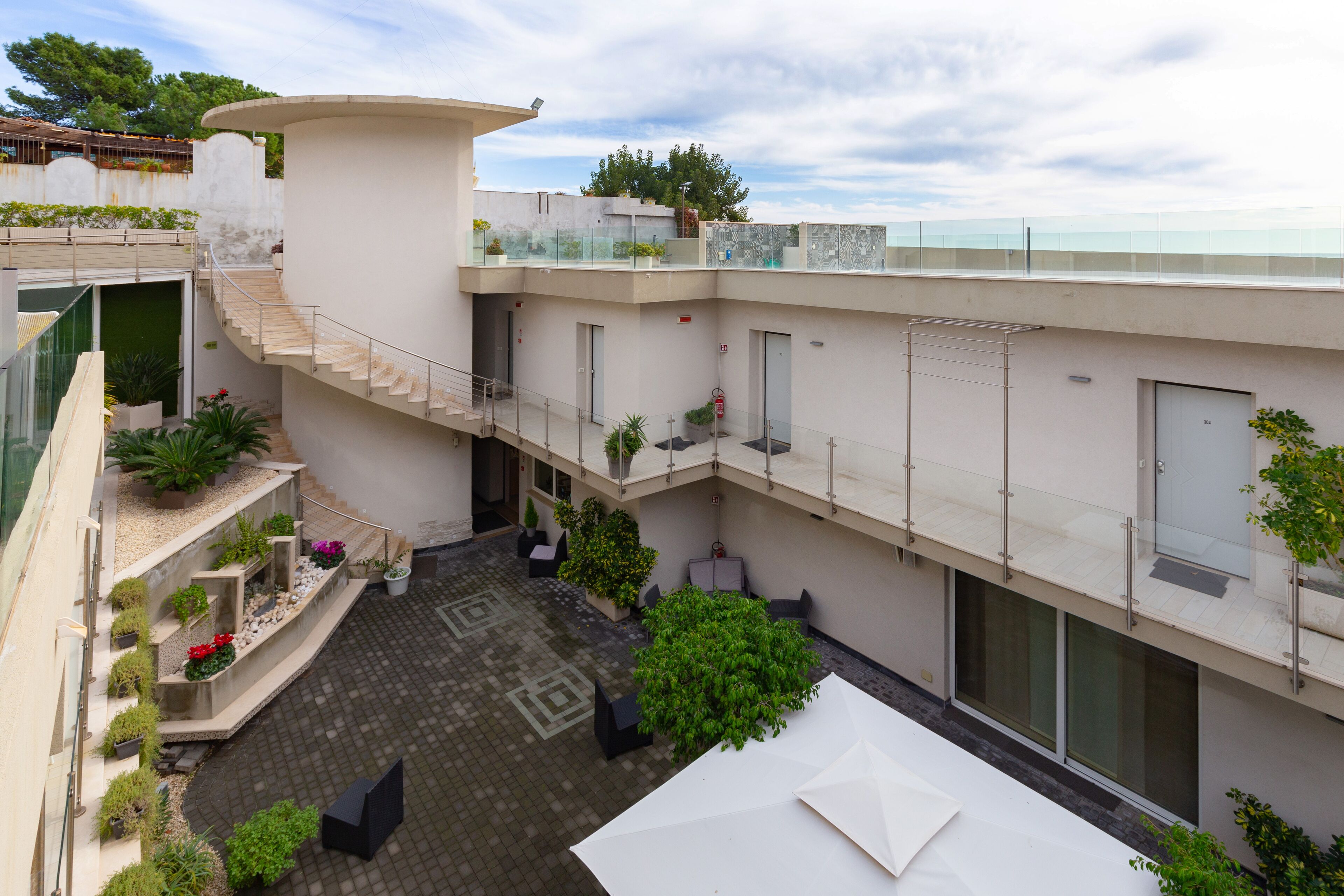 Un edificio moderno con un patio central, mobiliario exterior y una barandilla de vidrio que da a una masa de agua.