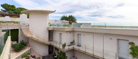 Un edificio moderno con un patio central, mobiliario exterior y una barandilla de vidrio que da a una masa de agua.