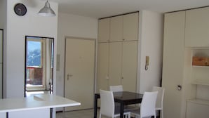 Un comedor con una mesa y sillas, un reloj en la pared, y una puerta que da a otra habitación.