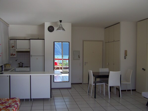Een kleine keuken met een eethoek, een groot raam met uitzicht, en een deur naar een andere kamer.
