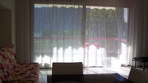 Habitación con sofá, una silla y una mesa. Cuenta con un ventanal con cortinas ligeras.