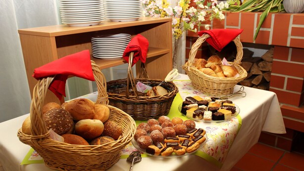 A table with baskets of bread and pastries, a set of plates, and a floral arrangement. - Acron Traben-Trarbach (Traben-Trarbach)