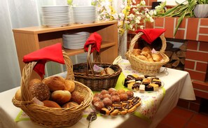 Une table avec des paniers de pain et de viennoiseries, une pile d’assiettes et un arrangement floral.