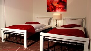 Two single beds with white frames and red-striped bedding, a wall-mounted lamp, and a red autumn leaf painting above the beds. - Acron Traben-Trarbach (Traben-Trarbach)