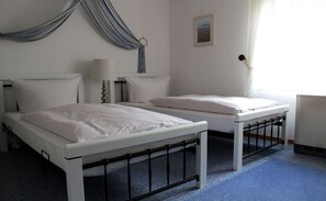 Une chambre avec deux lits, une table de chevet avec une lampe, une fenêtre avec des rideaux et un tableau au mur.