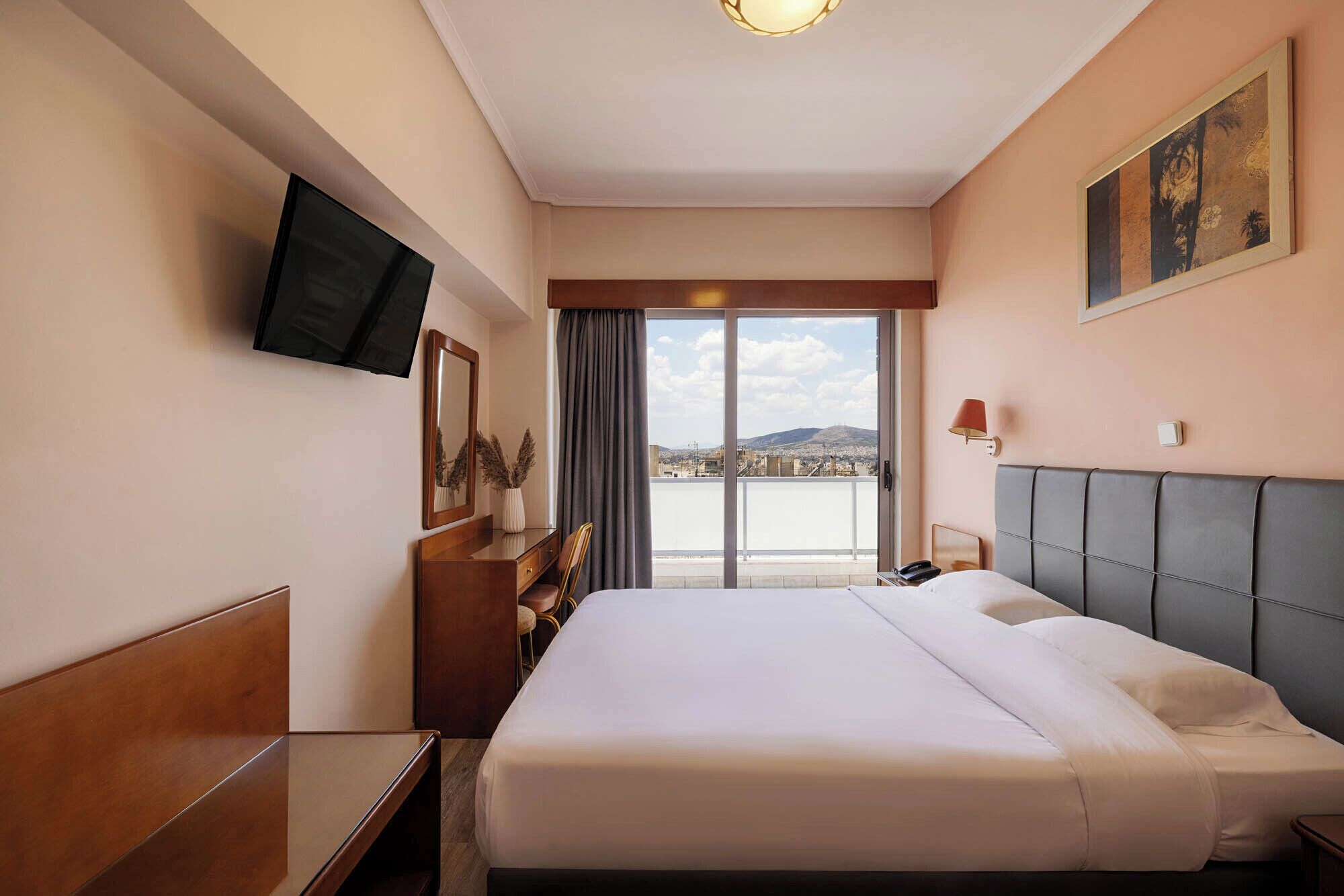Een hotelkamer met een bed, bureau, stoel, tv aan de muur, en een raam met uitzicht op de stad.