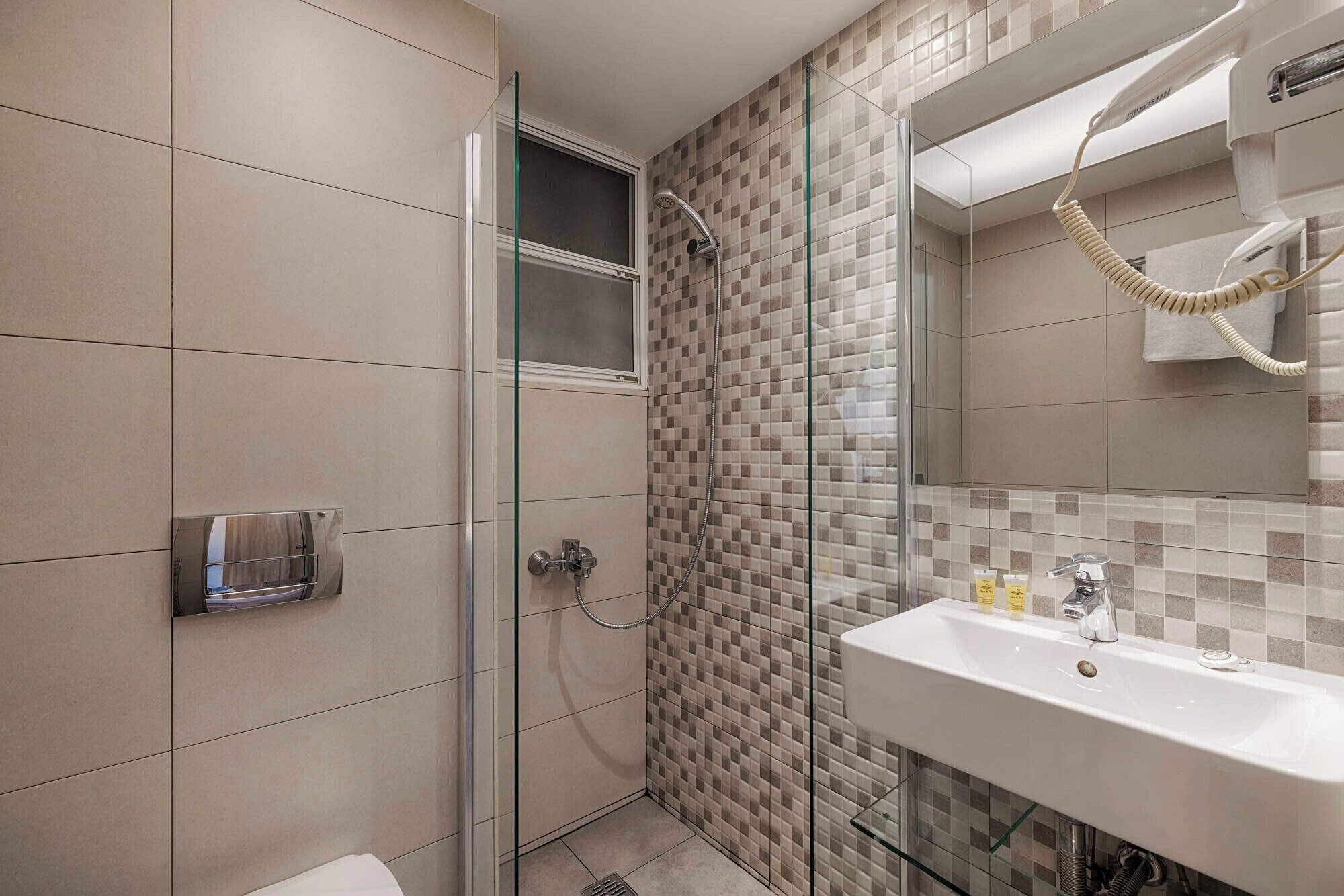 Un baño moderno con cabina de ducha de vidrio, un lavamanos blanco con artículos de aseo y un perchero para toallas.