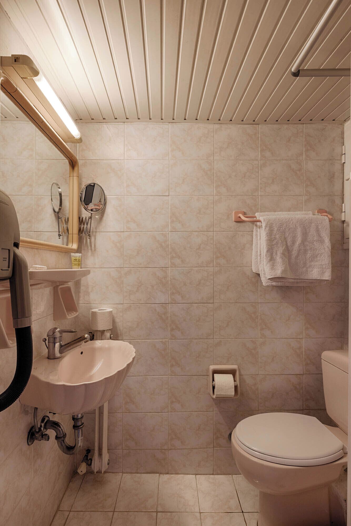 A bathroom with a sink, mirror, towel rack, toilet, and a shower area.