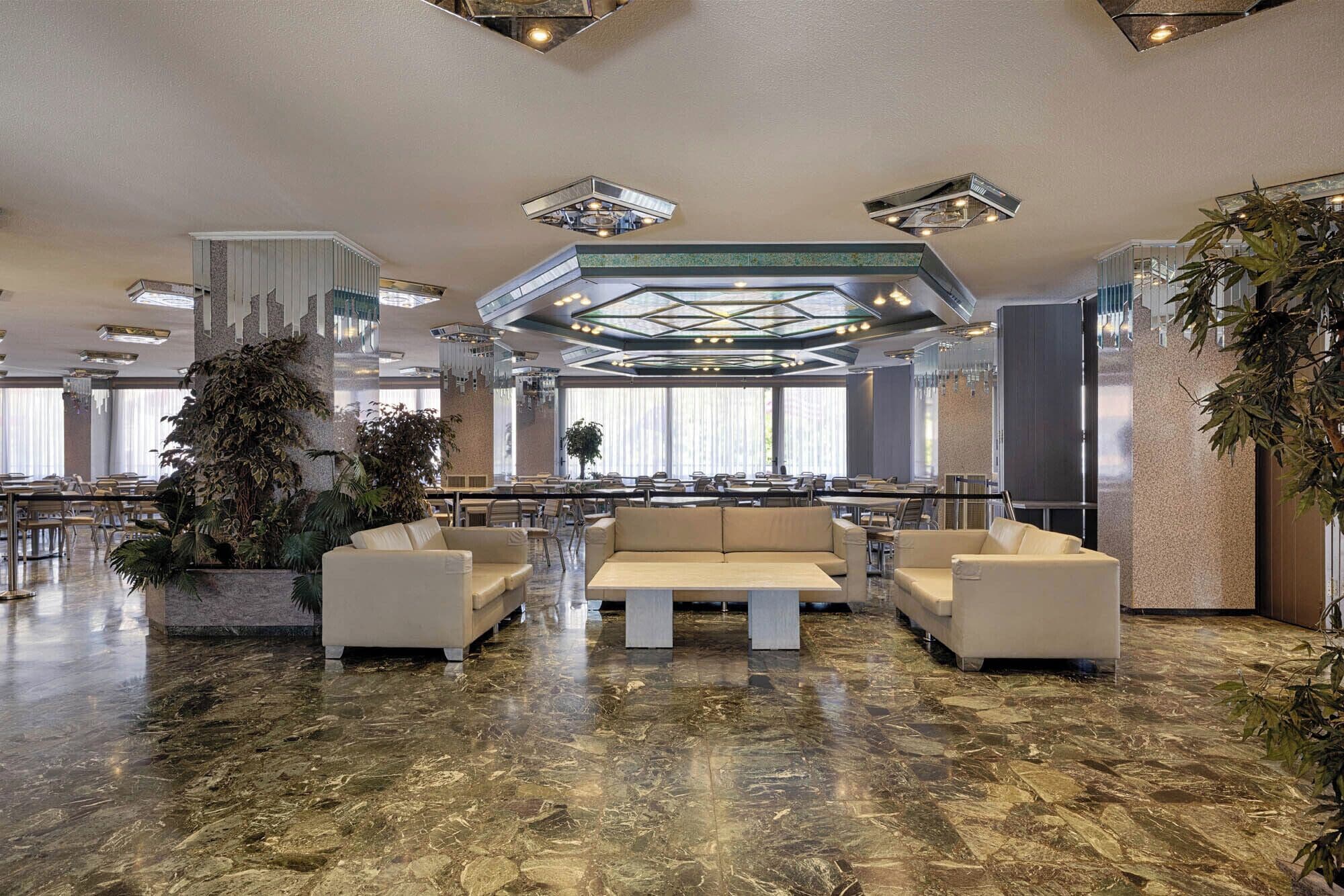 A spacious lobby with a central seating area, large windows, and a high ceiling with geometric lighting.