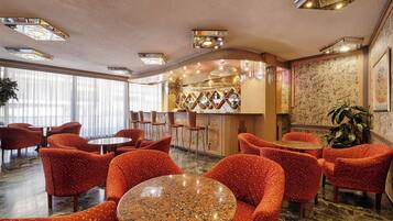 A hotel lobby with red upholstered chairs, a bar area, and a large window providing natural light.