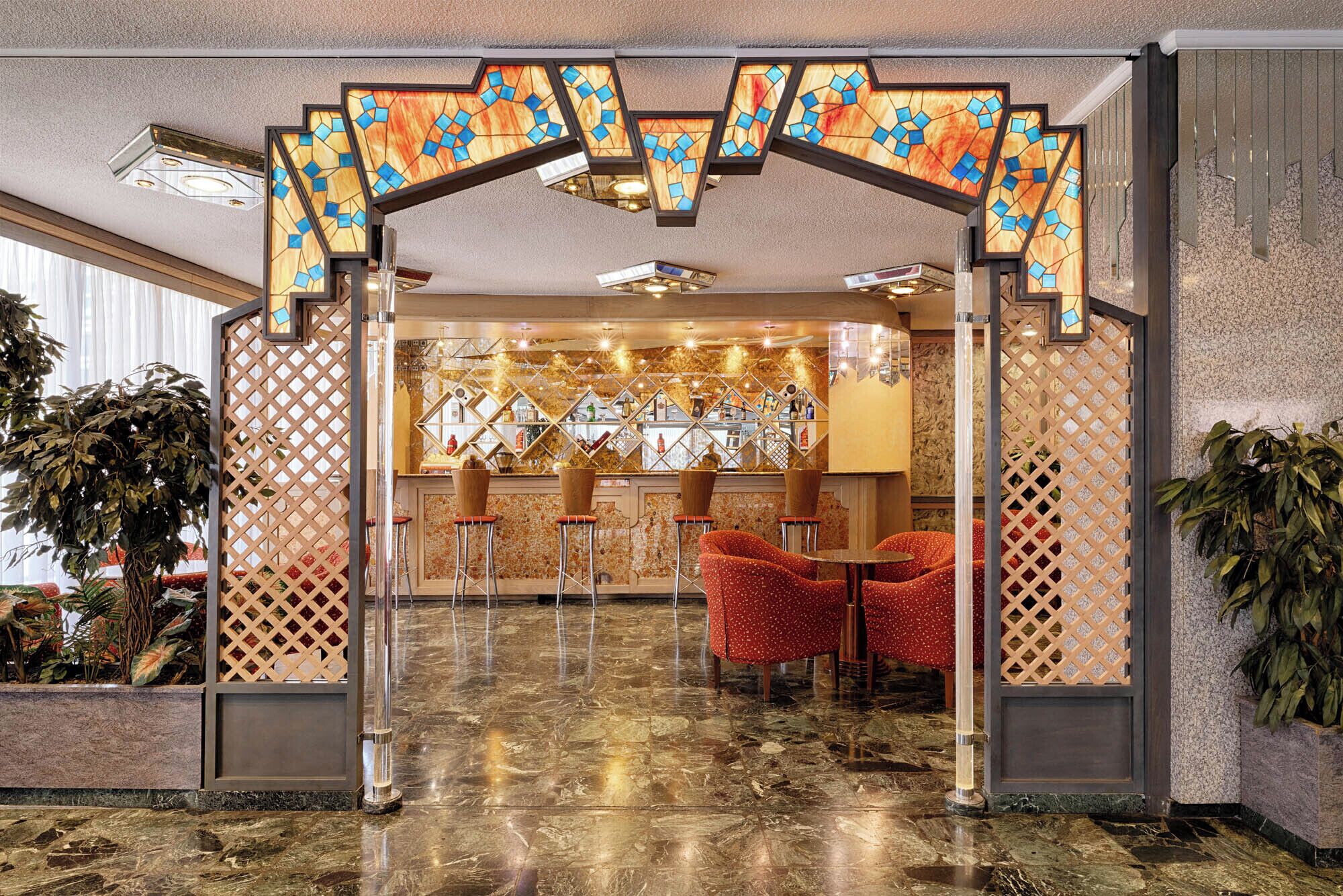 A lobby with a marble floor, a bar area with stools, and decorative glass panels.
