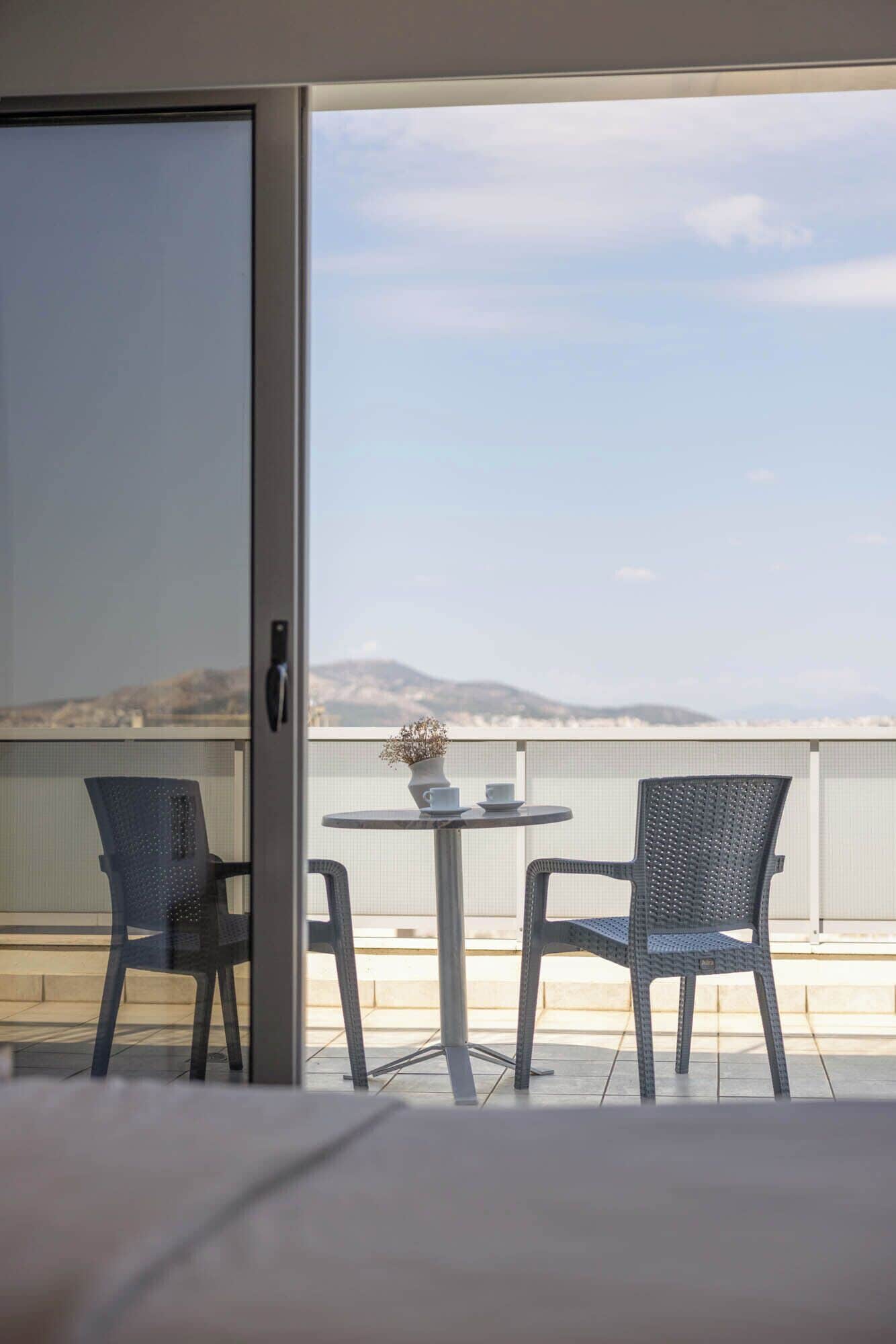 A balcony with two chairs and a table, overlooking a scenic view of a body of water and distant hills.