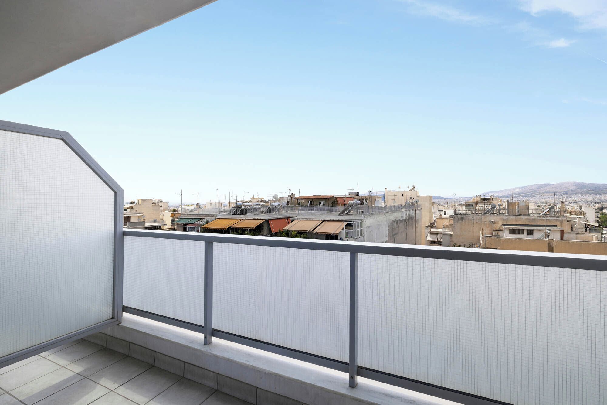 A balcony with a view of a cityscape, including buildings and a distant mountain range.