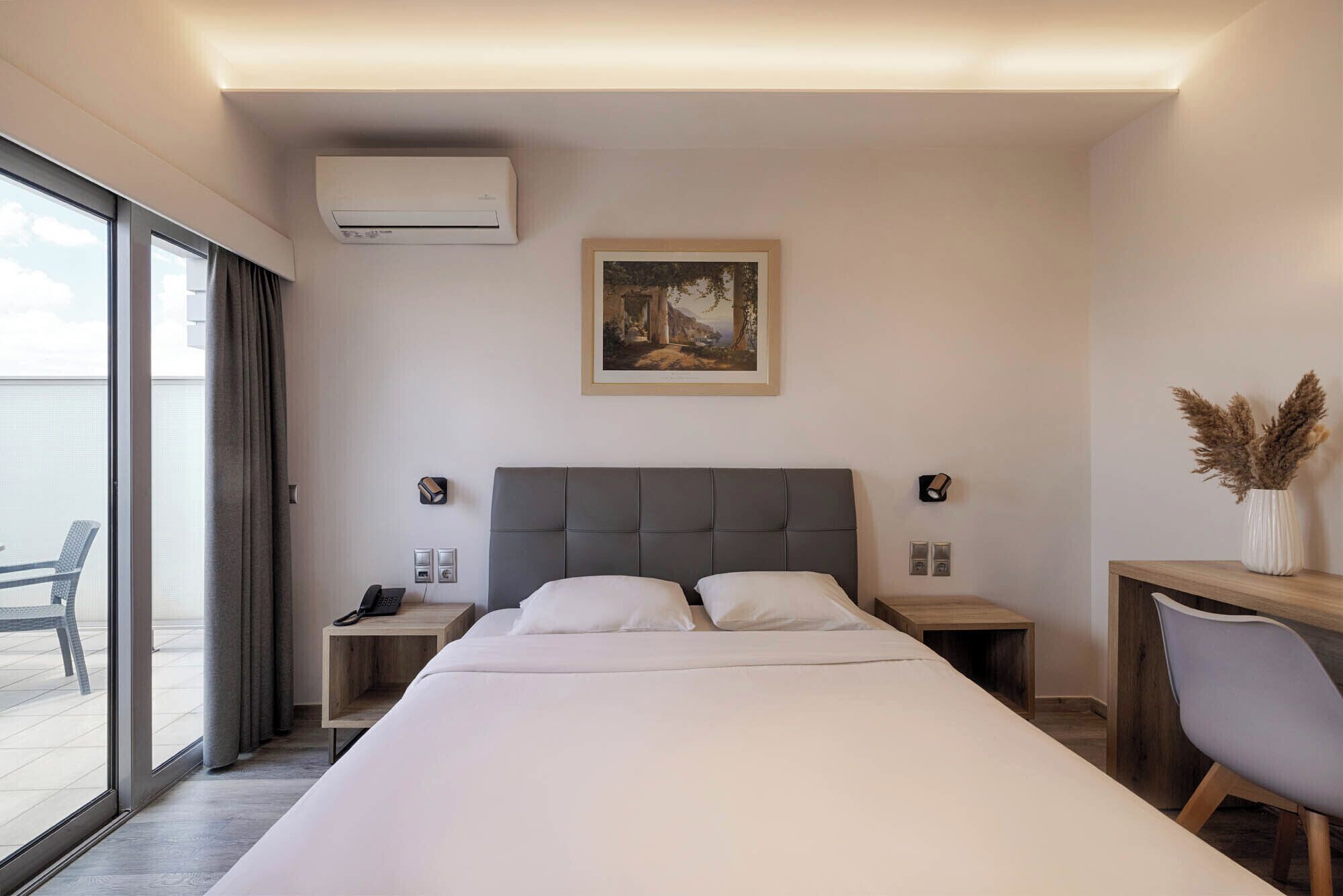 Une chambre d’hôtel avec un grand lit, un bureau, une chaise, un tableau au mur et un appareil de climatisation.