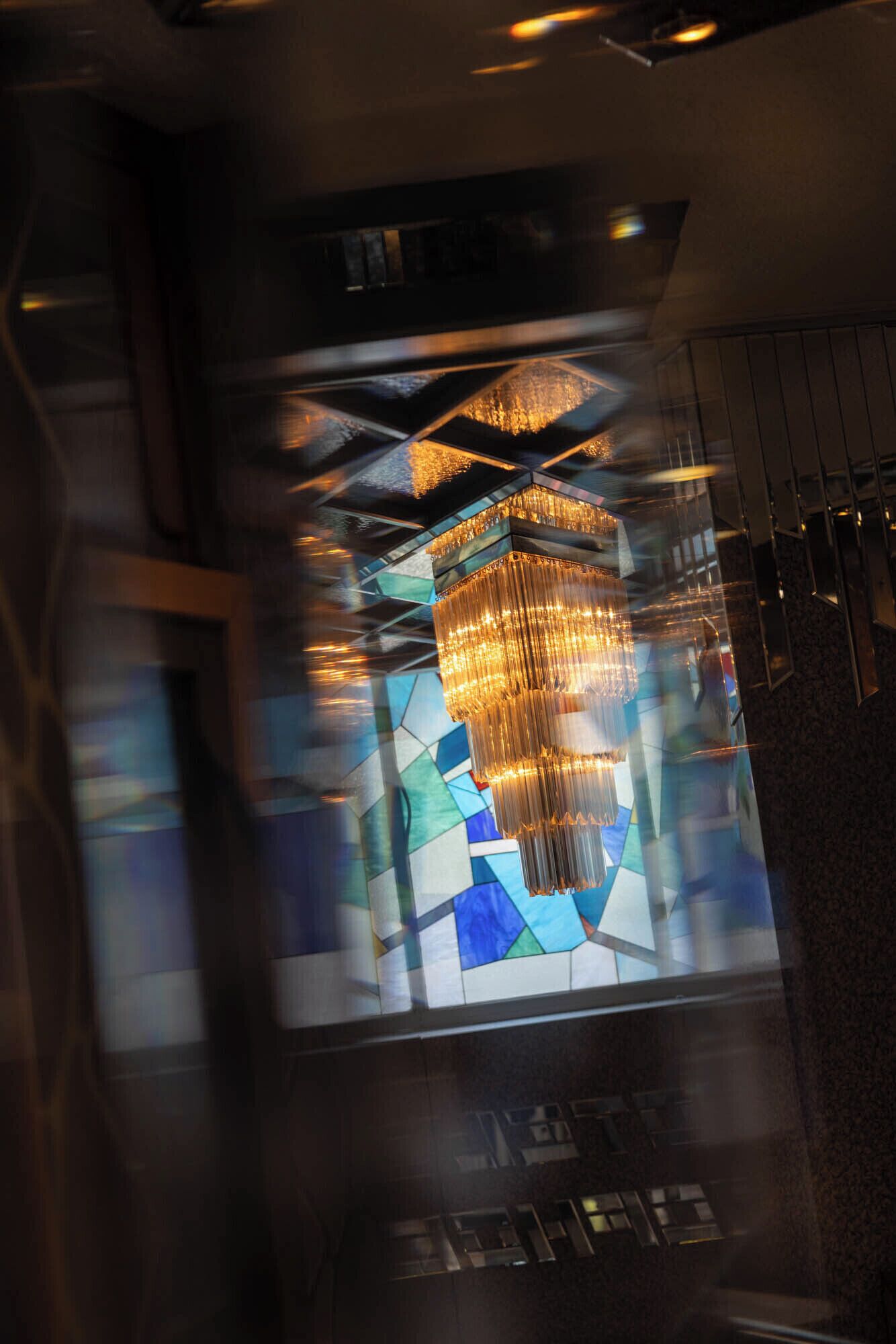 A chandelier with multiple tiers and a stained glass window with geometric patterns.