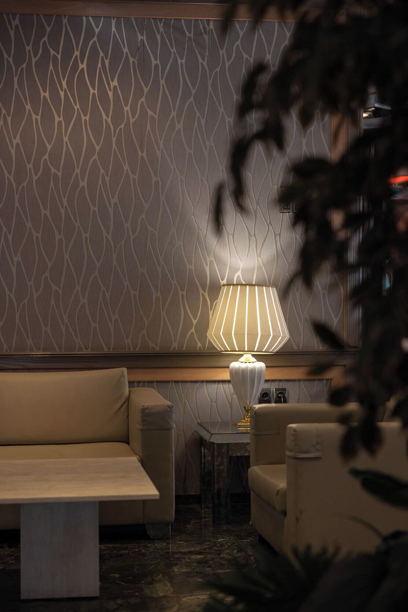 A modern interior with a patterned wall, a sofa, two armchairs, a small table, and a lamp.