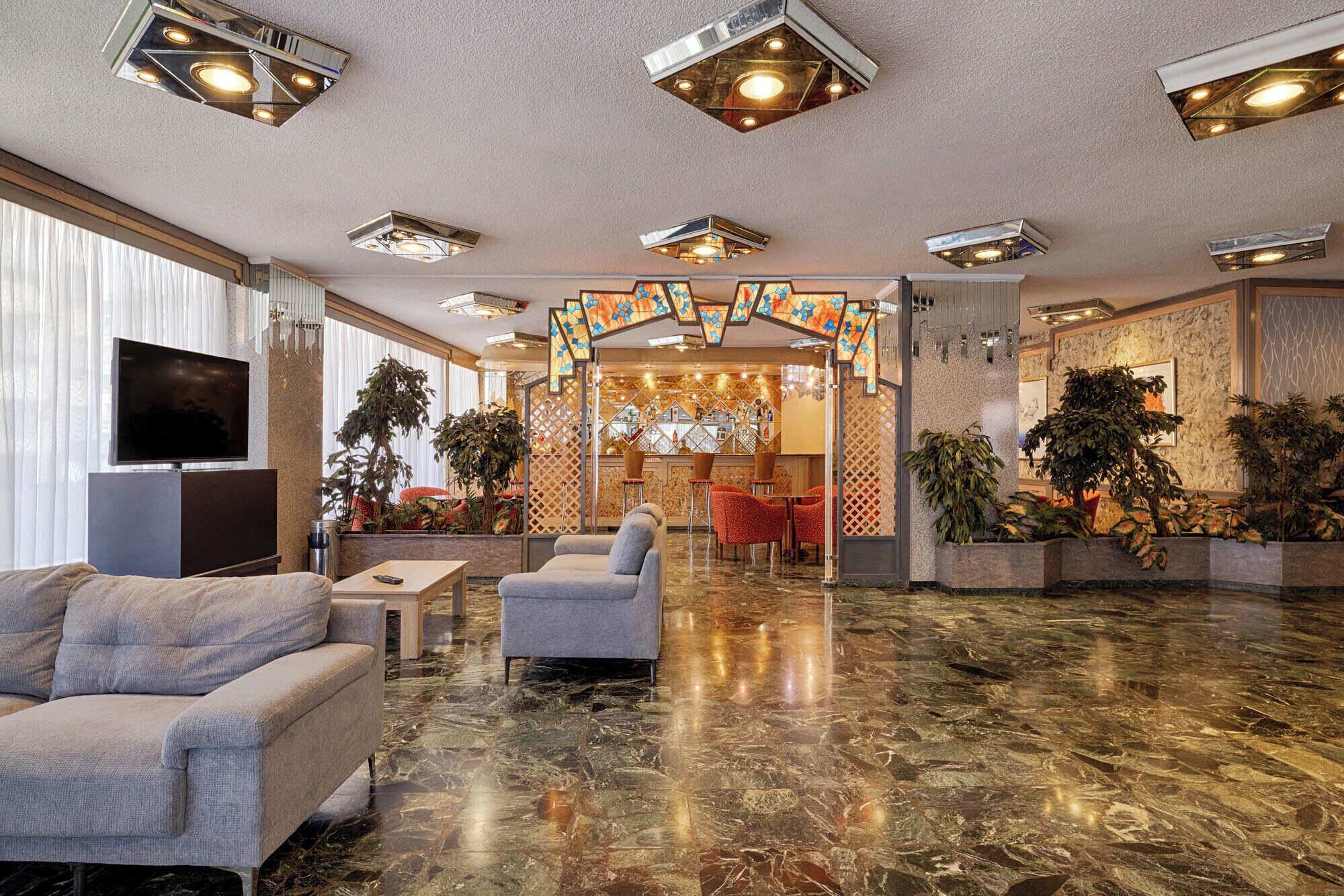 Un hall d’hôtel avec un sol en marbre, des canapés, un téléviseur et un coin bar équipé de tabourets.